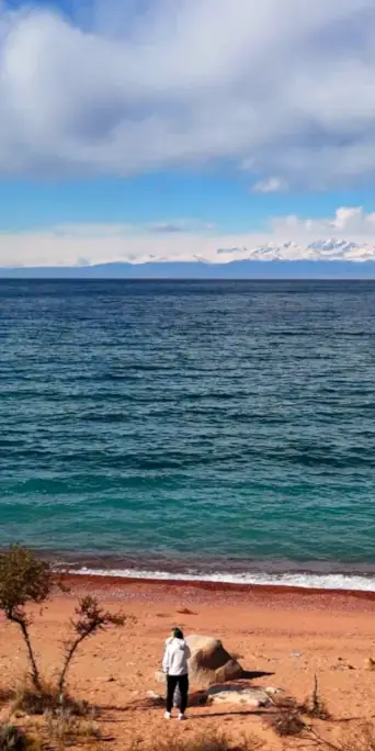 Золотистый пляж озера Иссык Куль с видом на снежные горные хребты