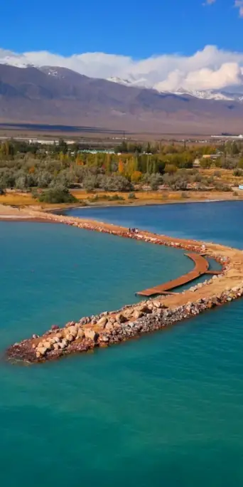 Вид с о озера Иссык Куль на городской пляж, горные пики и облака